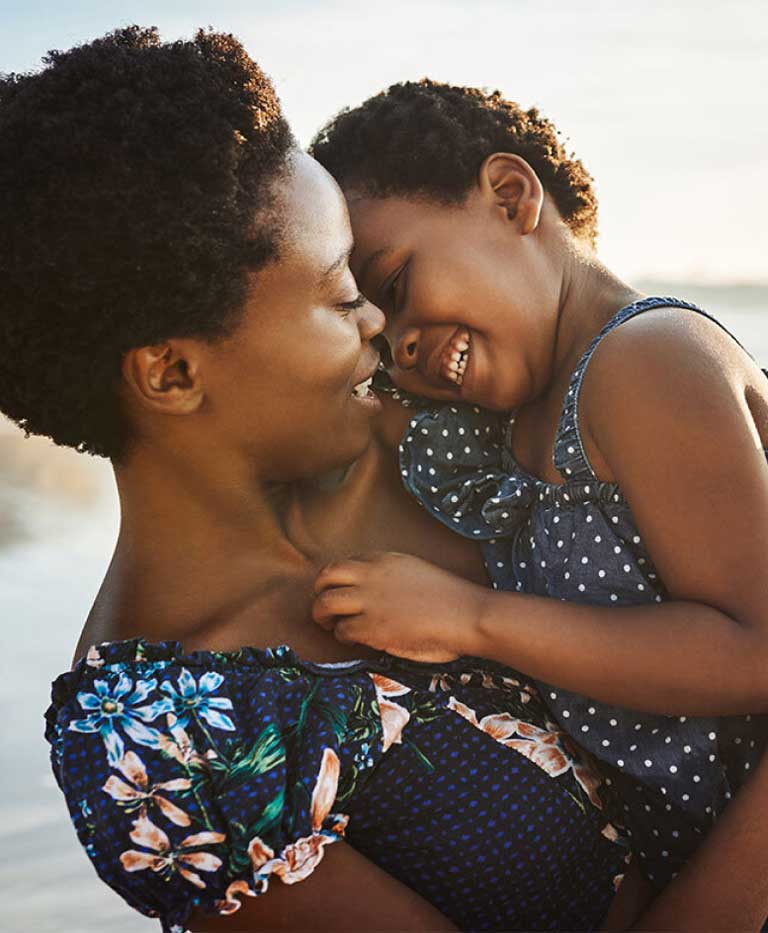 Smiling woman holding a happy young child with waves in the background