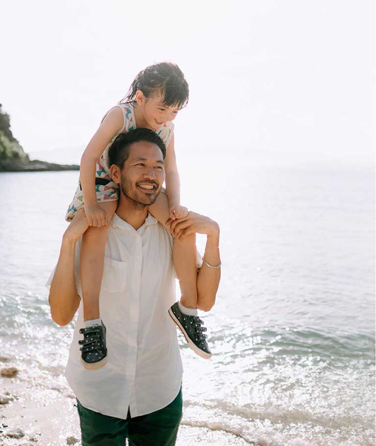 Smiling nan walking along the beach with a smiling young girl on his shoulders