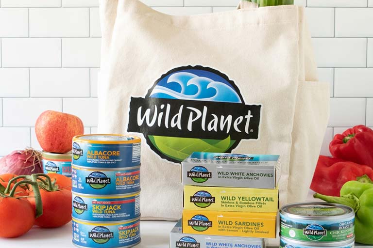 Wild Planet products on a countertop surrounded by fresh produce and Wild Planet reusable shopping tote