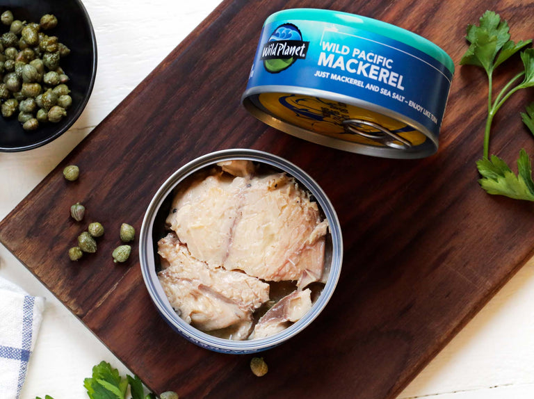 Wild Planet Wild Pacific Mackerel cans, one open, one closed, on a cutting board with fresh ingredients
