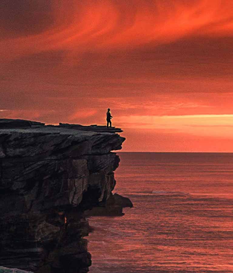 Beautiful orange and gold sunset over the sea with a person standing on a cliff in the distance