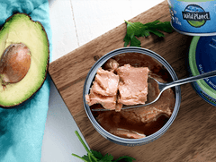 Fork in open can of Wild Planet Tuna on cutting board next to fresh avocado