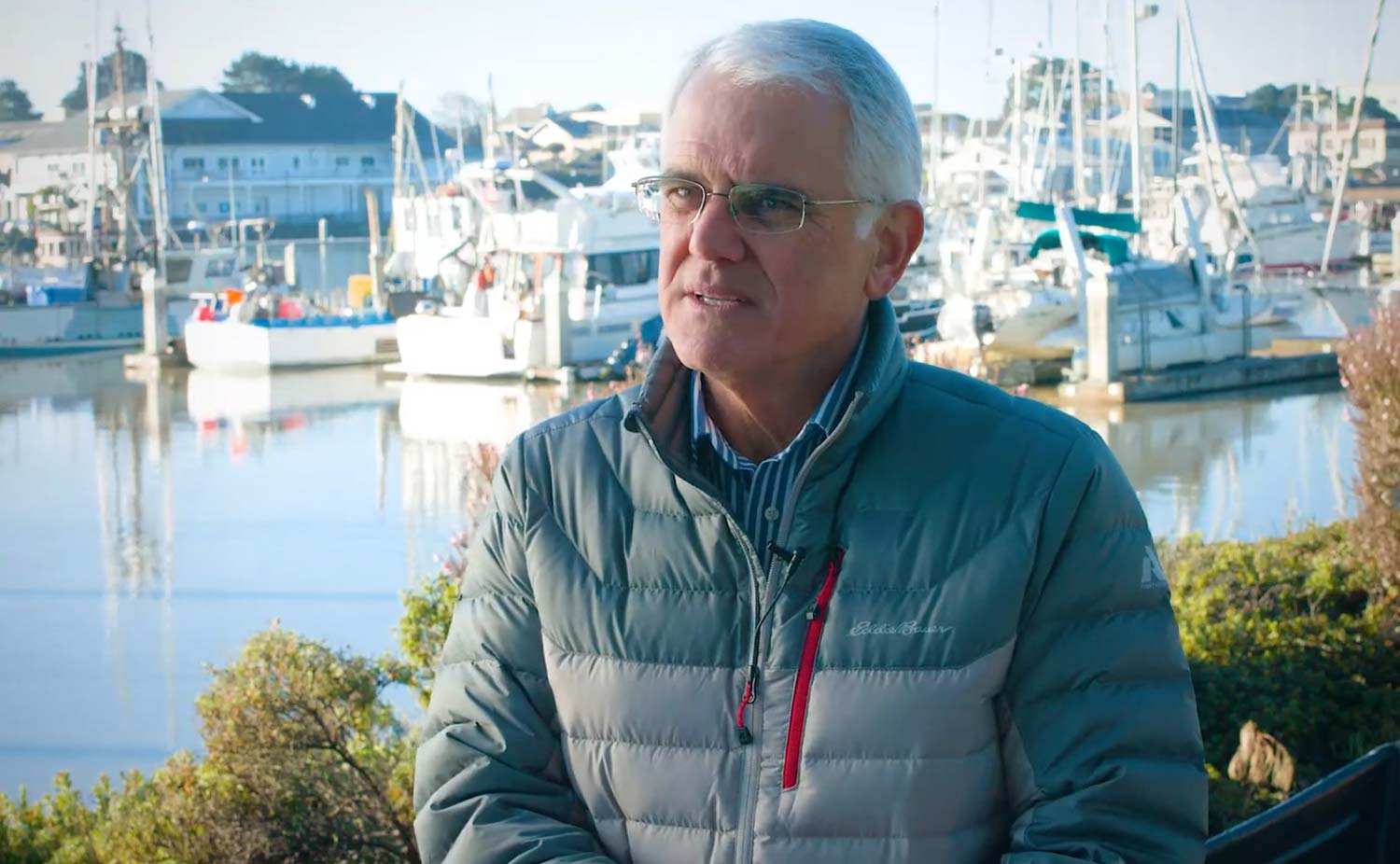 Wild Planet Foods Founder Bill Carvalho sitting outside with fishing vessels in the background.